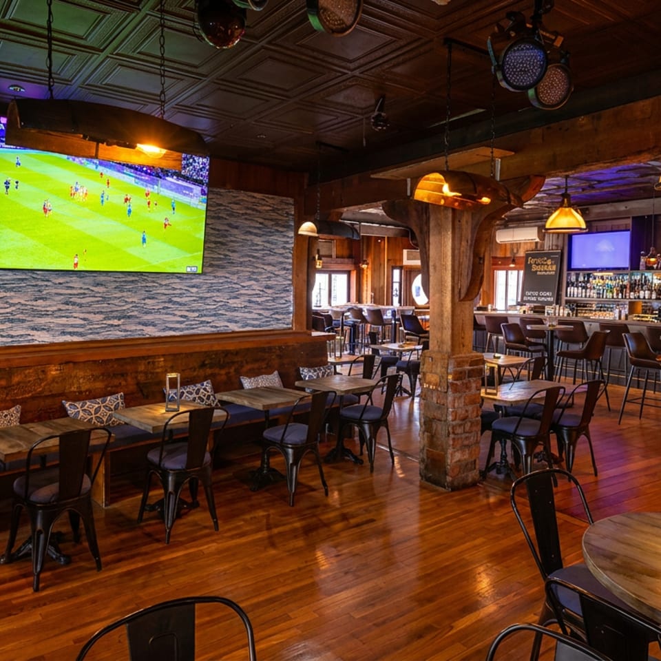 Spacious restaurant interior with a full bar, dining tables, and multiple TVs showing sports.